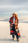 This long blanket-coat style duster is a truly elevated fashion piece. It has a bold aztec pattern of orange, red, and deep blue and hits about ankle length. The buttons are classic style conchos, and its so comfortable you won't want to take it off.   As with all of our pieces by Rhonda Stark Designs, this piece is handmade in the USA and the fabric comes directly from Italy. 