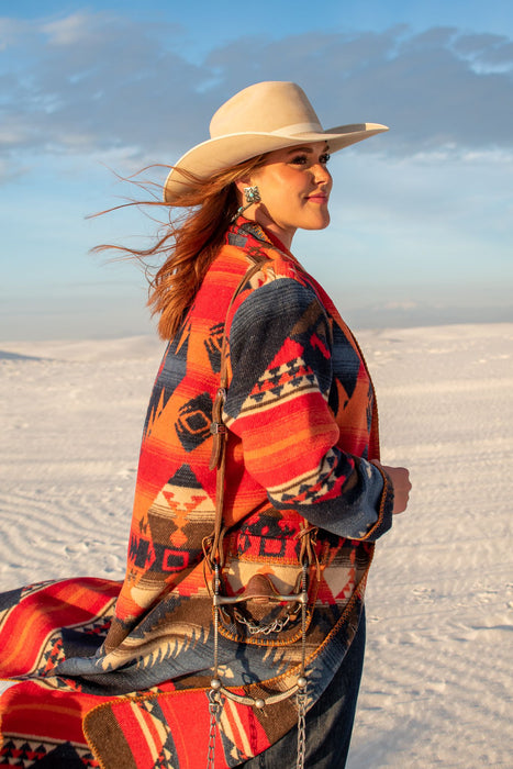 This long blanket-coat style duster is a truly elevated fashion piece. It has a bold aztec pattern of orange, red, and deep blue and hits about ankle length. The buttons are classic style conchos, and its so comfortable you won't want to take it off.   As with all of our pieces by Rhonda Stark Designs, this piece is handmade in the USA and the fabric comes directly from Italy. 